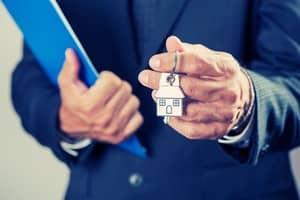 personne qui tient une clé de maison et une maquette de maison